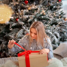 Teenage girl opening gift in front of tree | Date Your Spouse