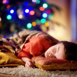 Child sleeping next to lit-up Christmas tree | Date Your Spouse