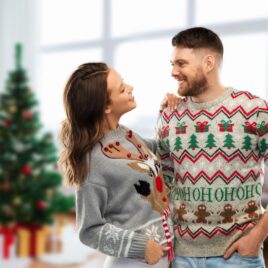 Couple wearing ugly Christmas sweaters in front of decorated tree | Date Your Spouse
