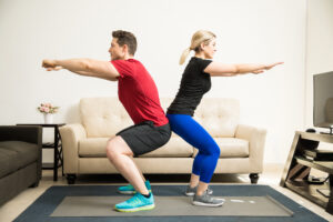 A couple squatting together at home - dateyourspouse.com A man and woman doing squats back-to-back at home | The Dating Divas
