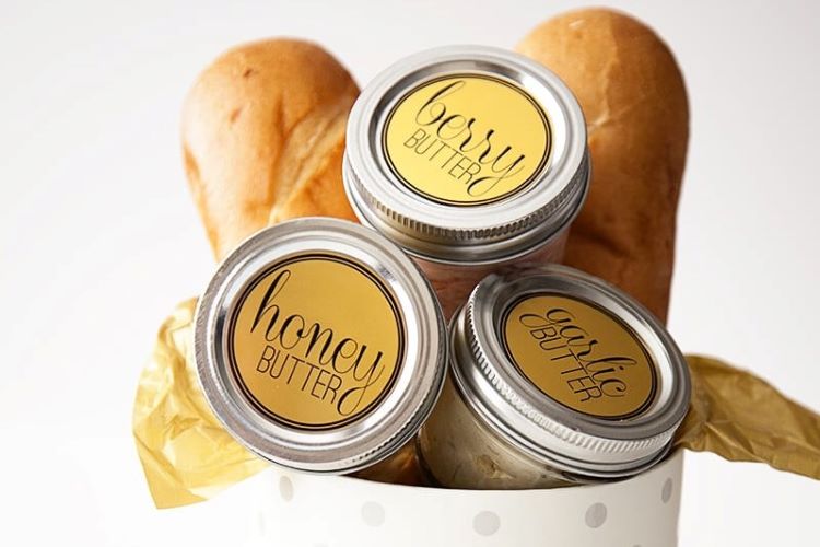 Homemade flavored butters in small jars alongside french bread - dateyourspouse.com A bread themed gift basket with three jars of flavored butter | The Dating Divas