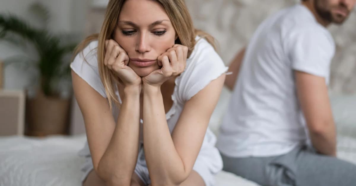 A wife with low desire in the bedroom looking sad and disconnected with husband in the background